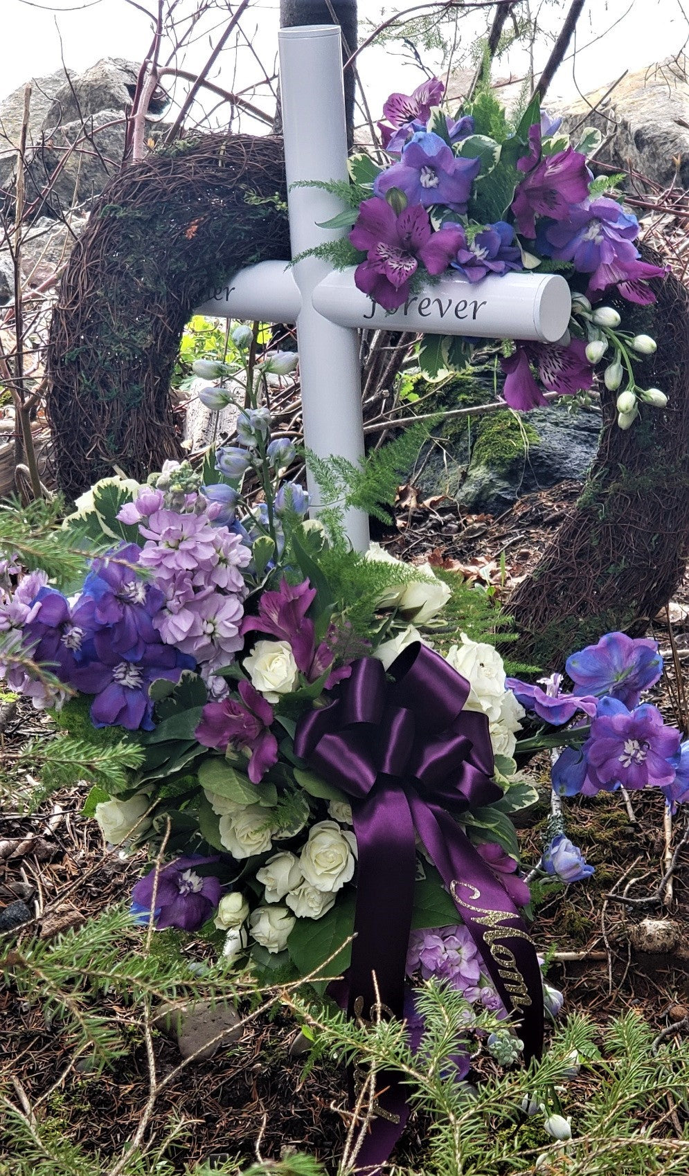 This White Everlasting Cross Memorial Is Placed In A Loved Ones Favorite Place. This Couples Unique Engraving Together Forever Represents the Love For Each Other. Memorial Was A Gift From Their Daughter, A Beautiful Heart Wreath and Purple Flowers hangs on their Tribute.